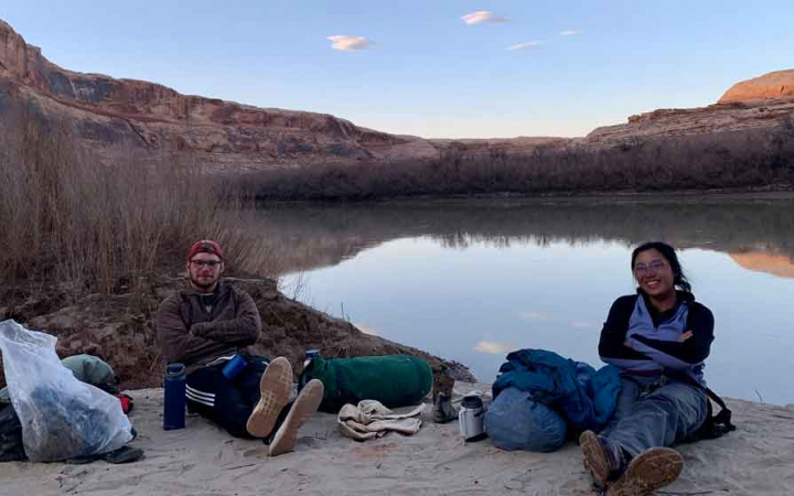 Two people rest on a rock beside a body of water in the Southwest